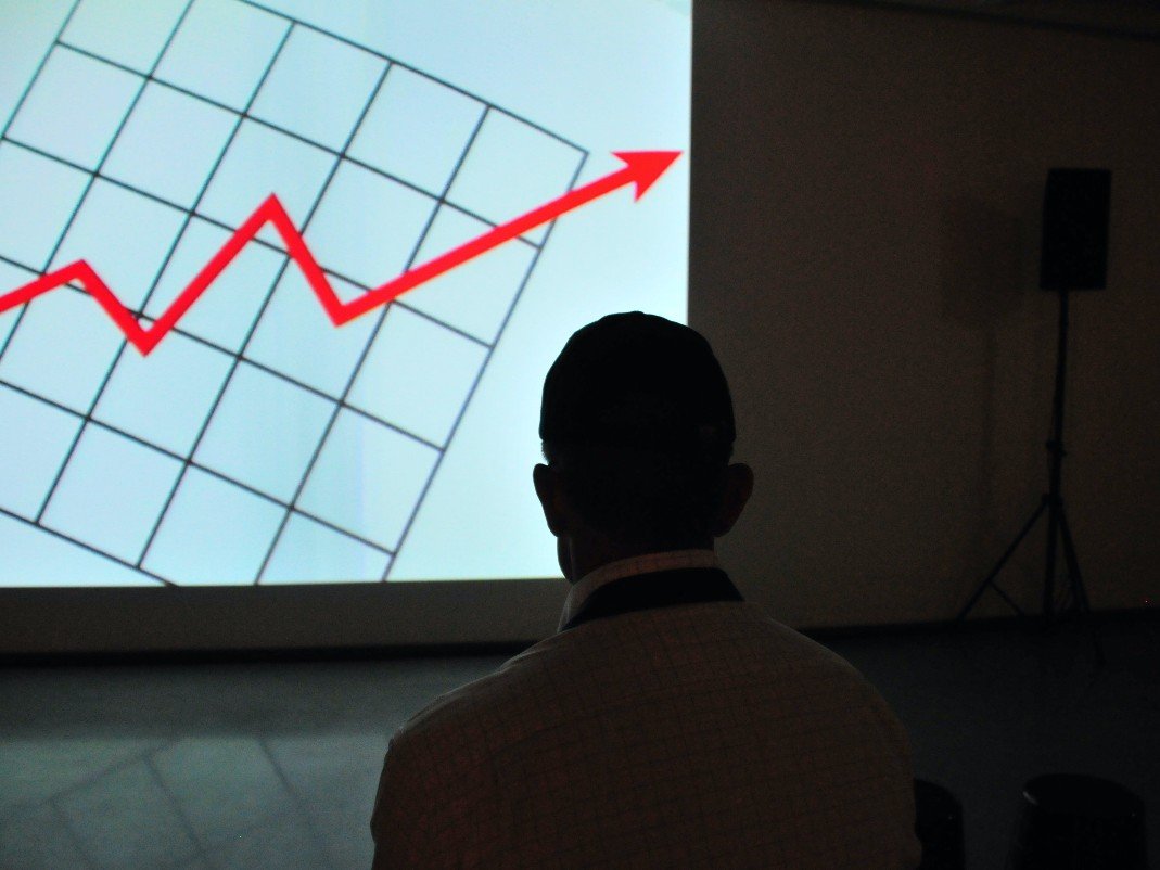Arrow pointing upward on a screen. A person watching a projected line chart trending upward